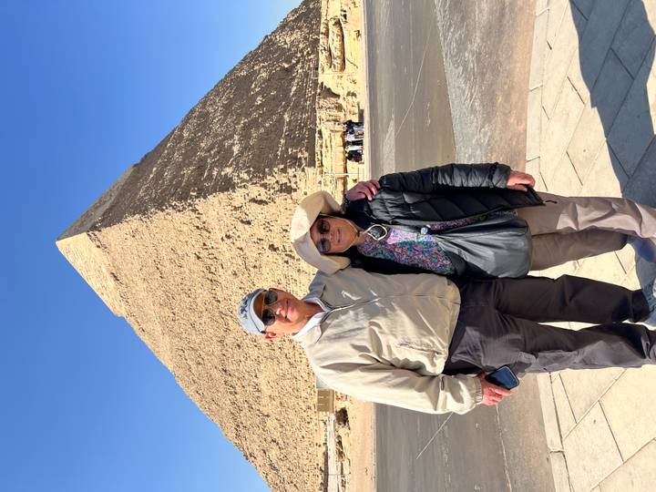Couple stands arm-in-arm before the Great Pyramid of Giza under a brilliant blue sky.