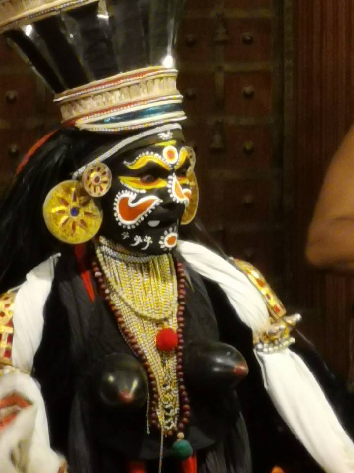 Blurred close-up of a performer in elaborate traditional face paint and ornate jewelry.