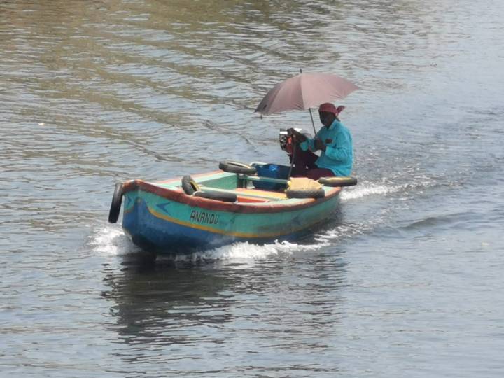 Man in a small painted motorboat holds an umbrella while navigating calm backwater canals.