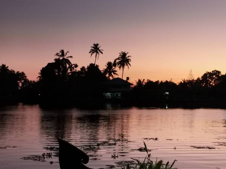 Palm trees and a house reflect in tranquil backwaters at sunset with an orange-pink sky.