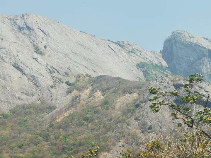 Steep rocky slopes of the Western Ghats with sparse vegetation under a pale blue sky.
