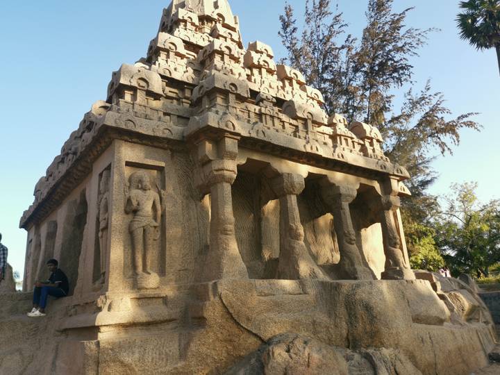 Granite monolithic temple of Pancha Rathas bathed in late afternoon light with visitors seated nearby.
