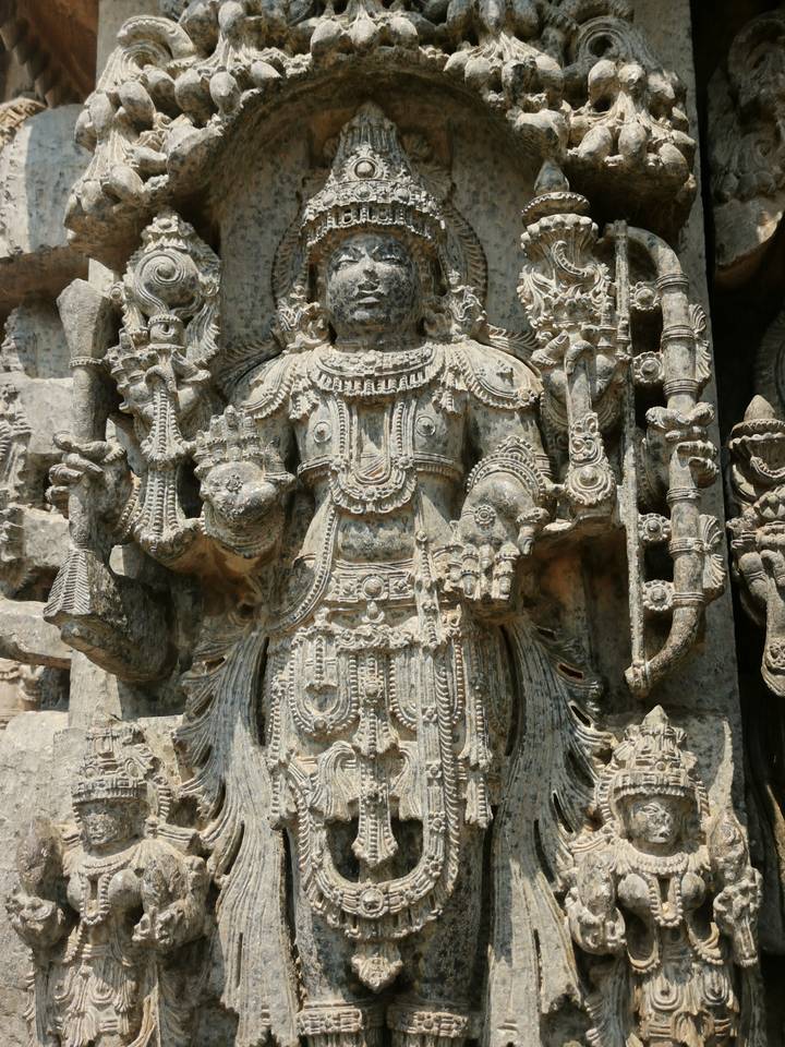 Intricate stone carving of a Hindu deity with ornate jewelry at an ancient temple.