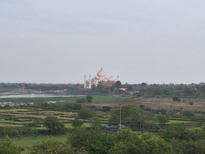 Distant view of the Taj Mahal across a river surrounded by flat countryside