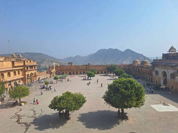 Elevated courtyard view of Amber Fort with visitors roaming wide plaza framed by Aravalli hills