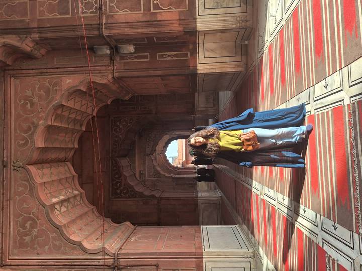 Traveler in long robe stands beneath ornate arches of a red sandstone mosque corridor