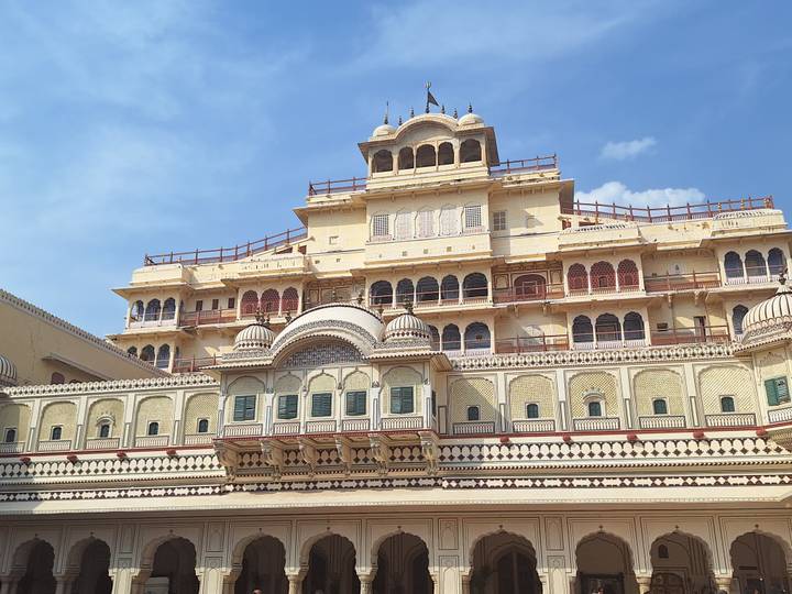 Facade of City Palace Jaipur with intricate balconies and cream-yellow walls under blue sky