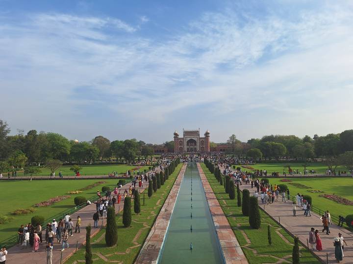 Symmetrical Mughal garden leading to red sandstone gateway near Taj Mahal with reflecting pool