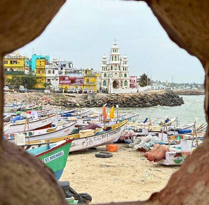 Colorful fishing boats line a coastal harbour with a white–green church tower and bright buildings in the background.