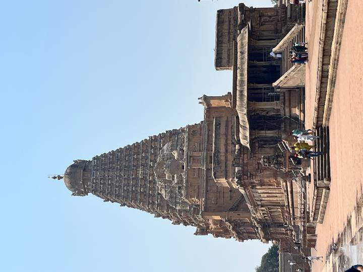 The towering Brihadeeswara Temple with visitors climbing the broad stone steps under a bright blue sky.