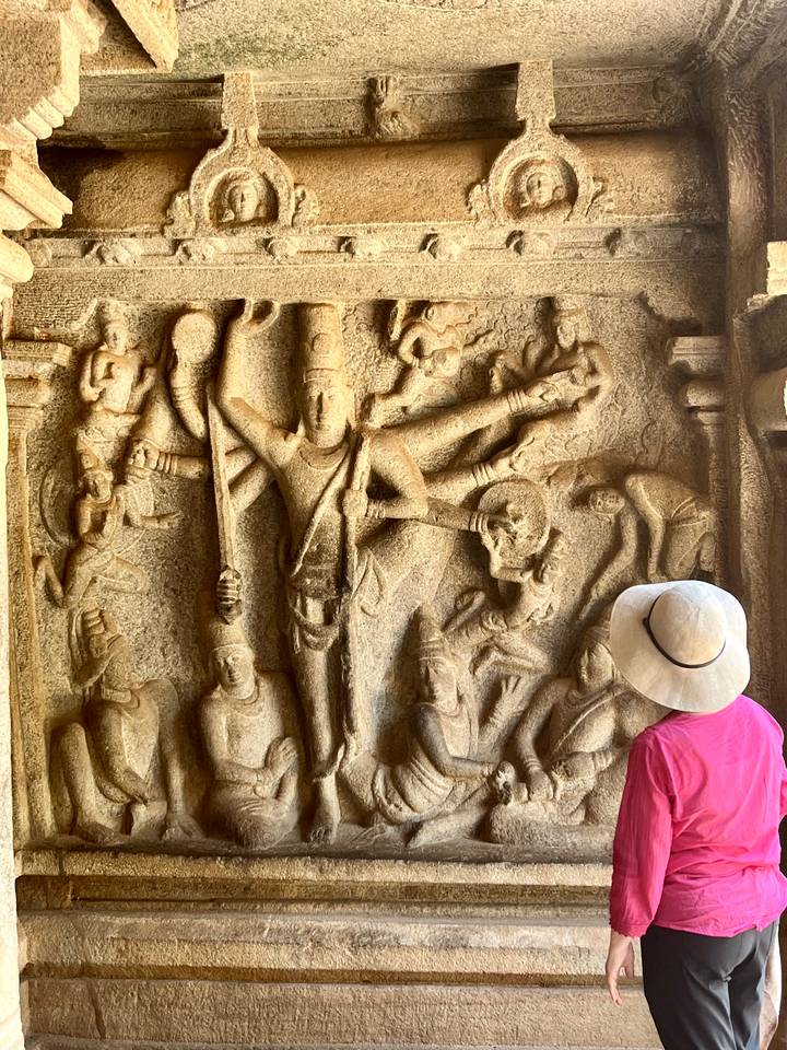 Traveller with sunhat admires intricate stone bas-relief of Hindu deities on an ancient cave wall.