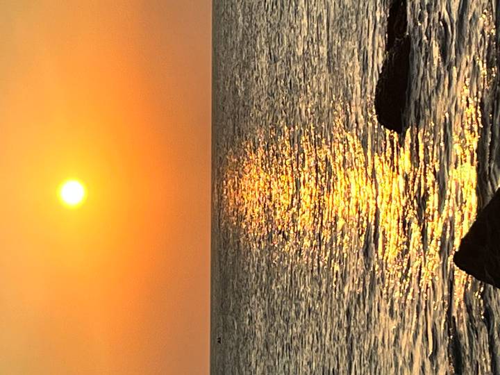 Brilliant orange sun sets over a calm sea casting a shimmering golden path on the water.