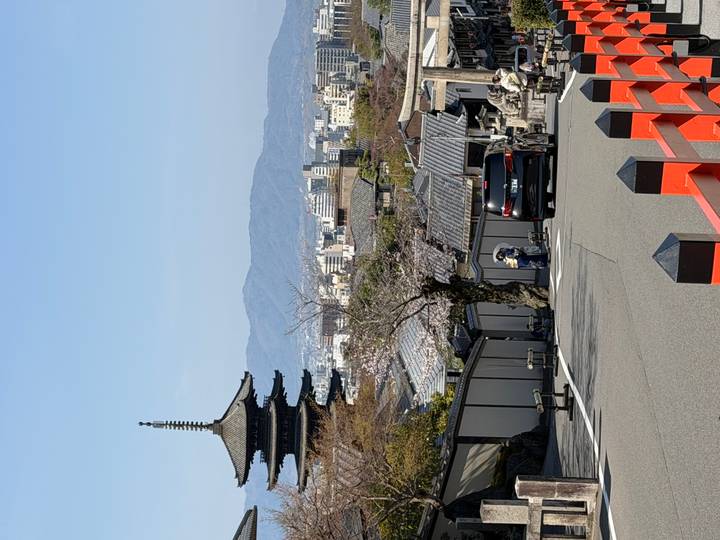 Yasaka five-storey pagoda rises above rooftops with mountains and cityscape in the distance.
