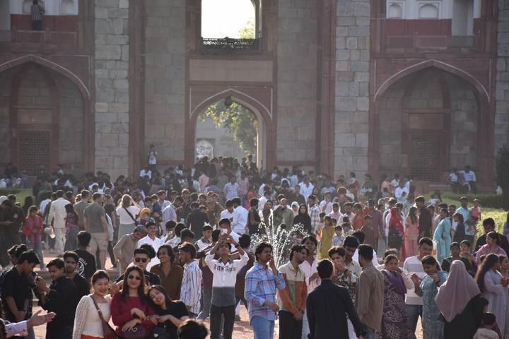 Dense crowd of visitors gathers at the entrance arches of a historic monument in Delhi.