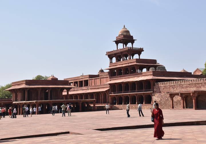 Wide courtyard view of the red-sandstone Panch Mahal at Fatehpur Sikri with visitors walking across the square.