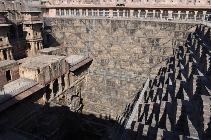 Deep geometric stone stepwell with intricate symmetrical stairs and pavilion niches.