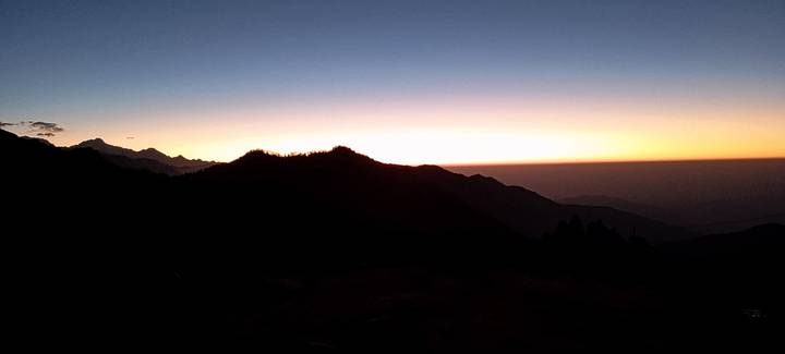 Silhouetted ridgeline at first light with golden horizon and dark valleys below.