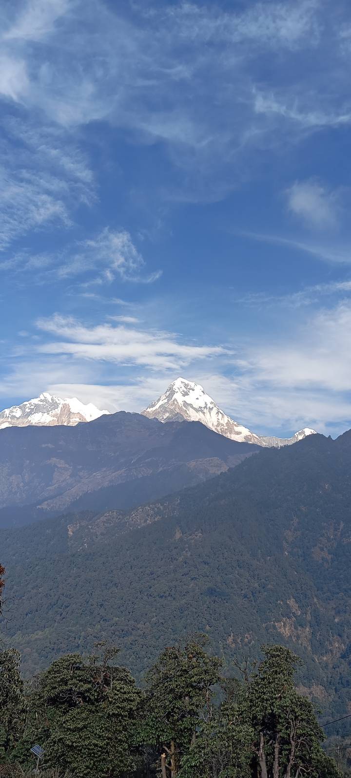 Close-up of a snow-covered Himalayan peak under a blue sky with wispy clouds.