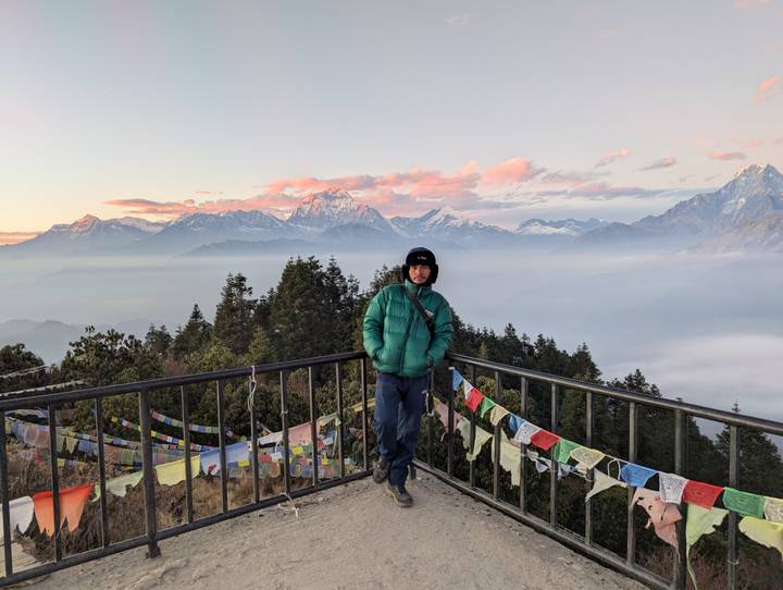 Traveller stands on a lookout deck festooned with prayer flags, above a hazy Himalayan vista.