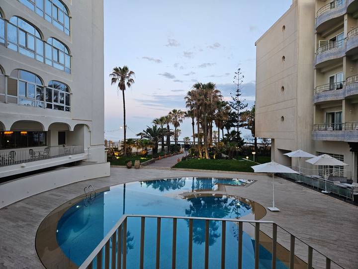 Hotel pool courtyard with palm trees overlooking the sea at twilight.