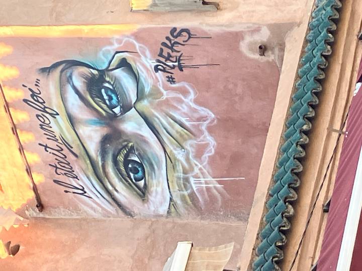 Colorful street-art mural of expressive eyes with Arabic-French script on wall.