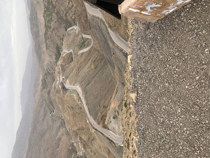 High-altitude serpentine road winding through barren brown mountains on an overcast day.