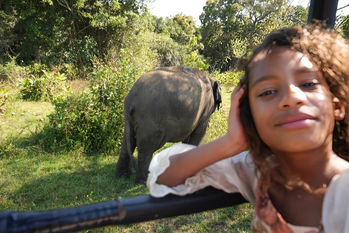 Close shot of a smiling girl on a safari jeep with an elephant grazing in the background.