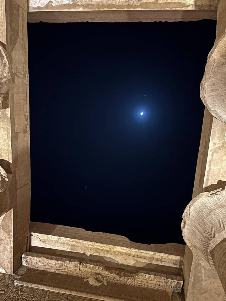Night sky with bright moon framed by two massive stone columns in darkness.