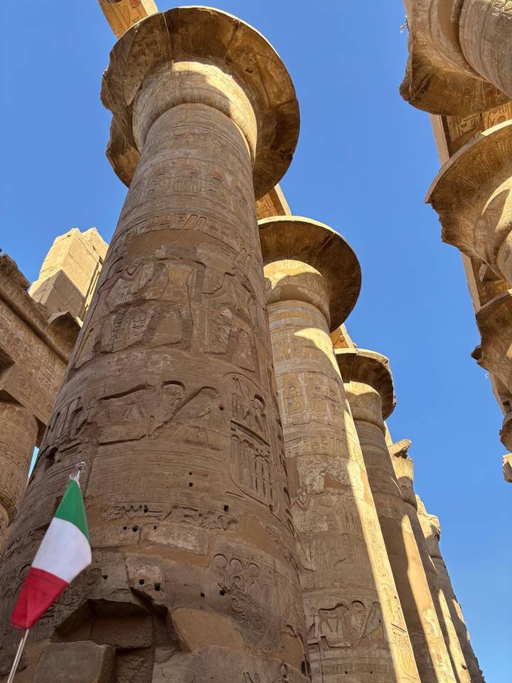 Massive carved sandstone columns with hieroglyphs at Karnak Temple under clear blue sky.