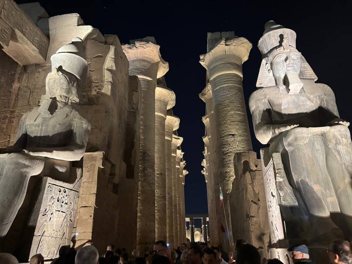 Nighttime view between colossal seated statues and towering columns at Luxor Temple.