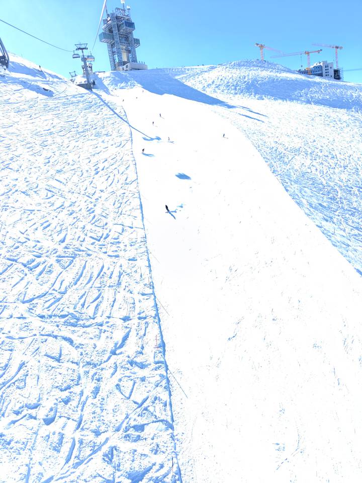 Top-down view of an overexposed snowy ski slope with a few skiers descending.