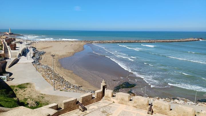 Sweeping coastal view of golden sand beach, breakwater and turquoise Atlantic under cloudless sky from ancient ramparts.