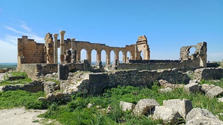 Well-preserved Roman basilica ruins with arches and standing columns set against a bright blue sky.