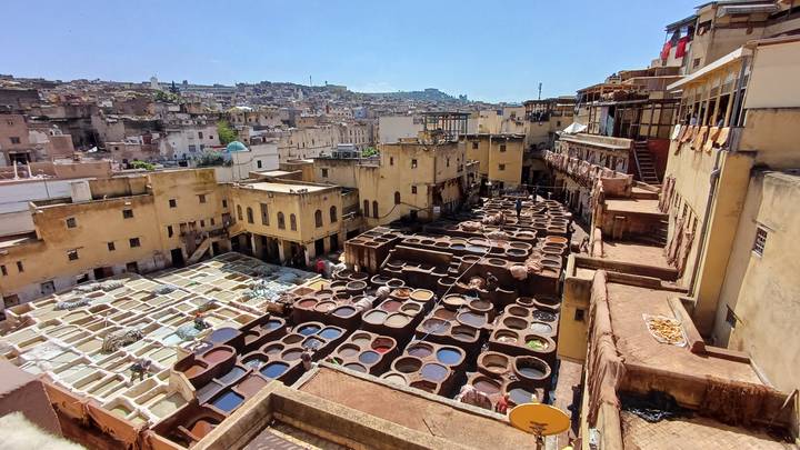 Panoramic view over Fes tanneries with hundreds of colourful dyeing vats and surrounding cityscape.