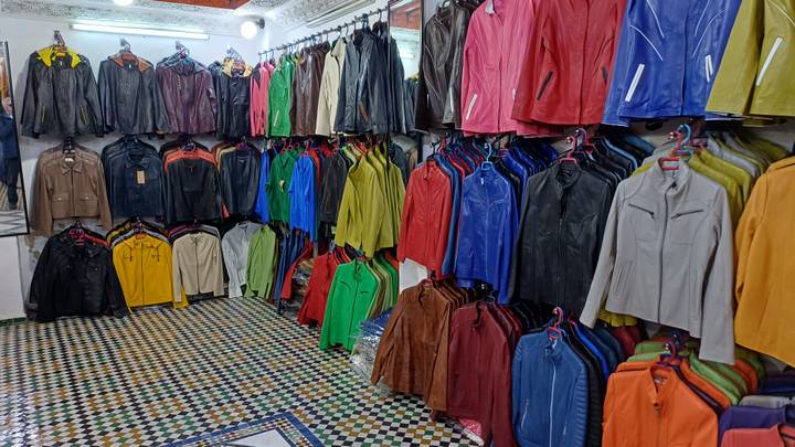 Colourful leather jackets neatly displayed on racks above patterned mosaic flooring in a shop.