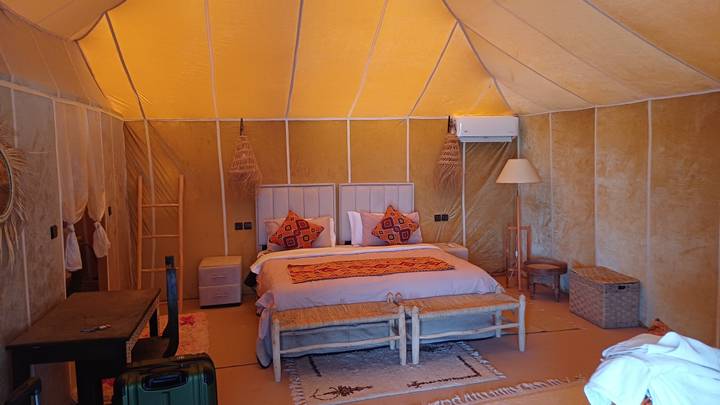 Interior of a stylish desert tent featuring a cosy bed, patterned rug and woven decor.