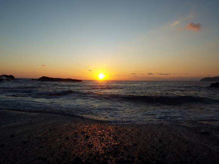 Serene ocean sunset with golden sun dipping below the horizon casting reflections on gentle waves.