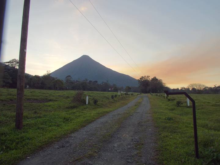 Conical volcano rising above grassy pasture at dusk with pastel sky hues and country road.