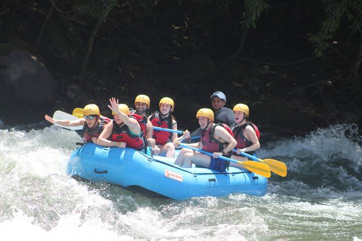 Thrilled rafters in a blue inflatable navigating white-water rapids surrounded by lush jungle.