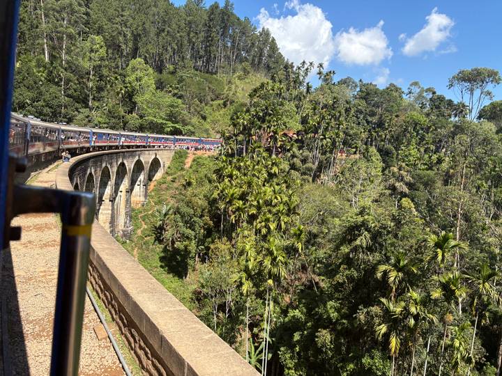 Long blue train curving across the famous Nine-Arch Bridge amid lush forest