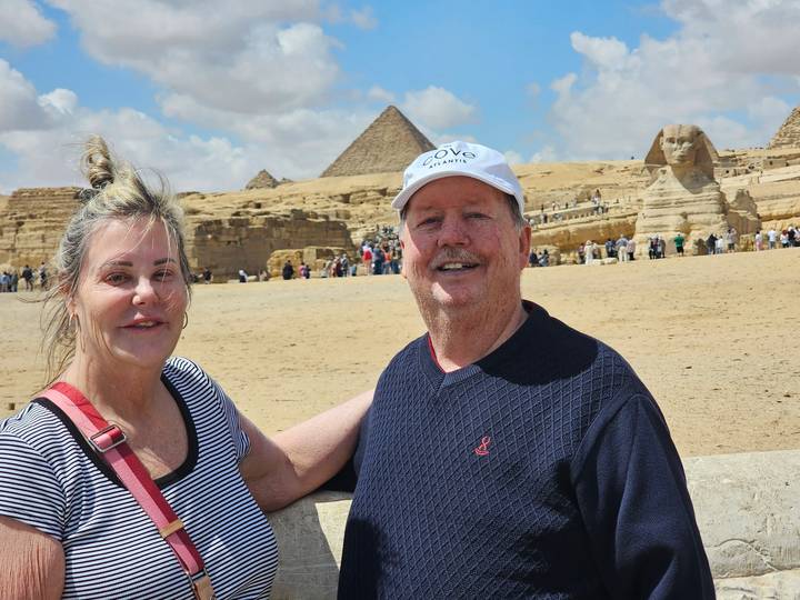 Smiling couple posing with Great Pyramid and Sphinx in sandy Giza plateau