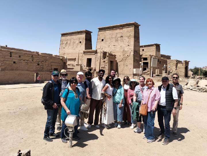 Tour group posing in front of sandstone pylons and hieroglyphs at ancient Philae Temple