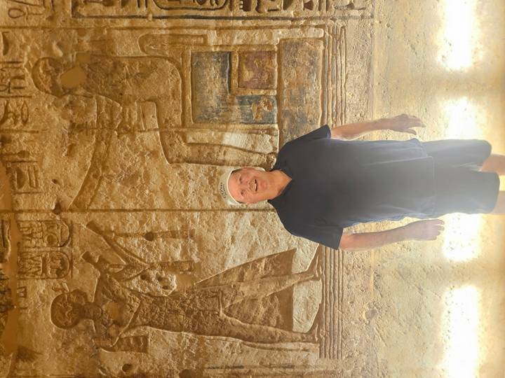 Traveller standing before illuminated ancient relief carvings inside Egyptian temple chamber