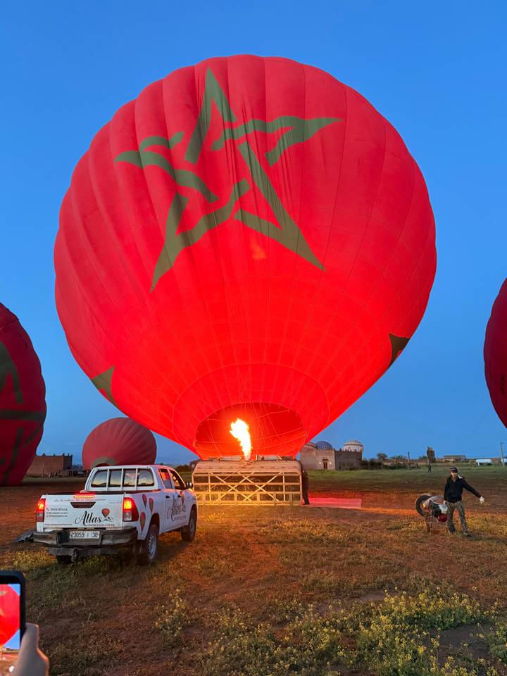 Bright red hot-air balloon with green Moroccan star as flame ignites during predawn inflation