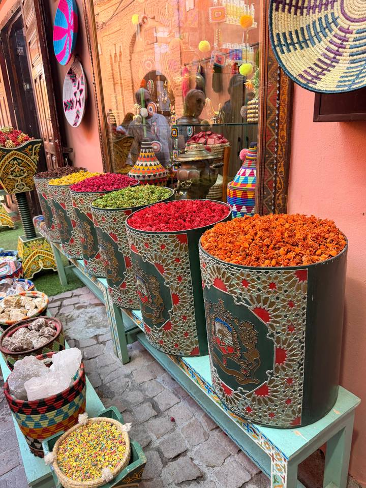 Row of ornate metal barrels overflowing with brightly colored dried spices in a Moroccan souk