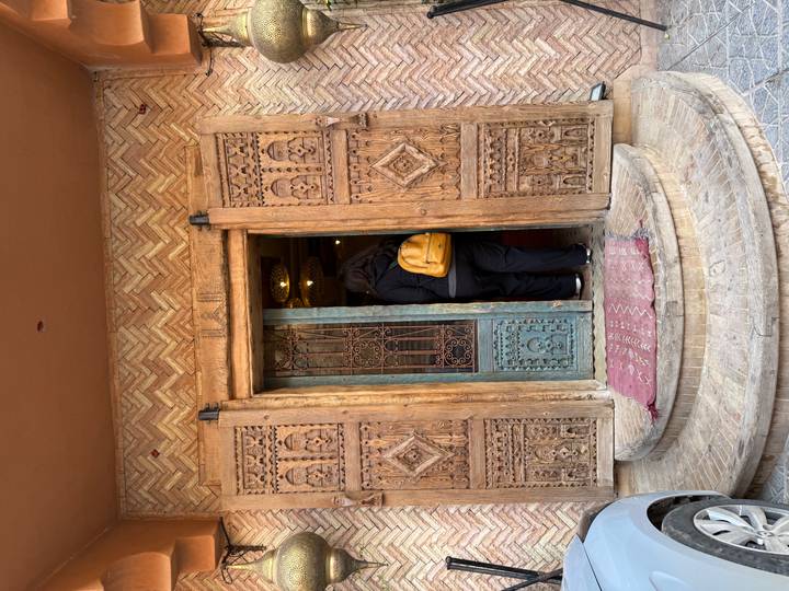 Traveler with yellow backpack entering a rustic carved wooden door of a traditional building