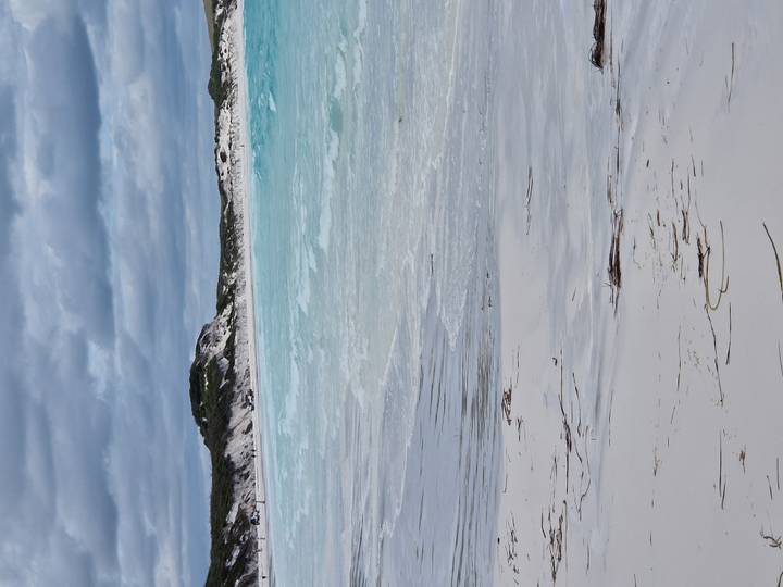 Pristine white-sand beach with turquoise waves and dunes beneath an overcast sky.