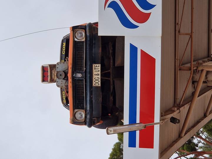 Old rust-colored ute mounted on a service-station roof with humorous licence plate.