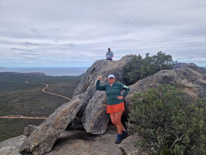 Hikers posing on a rocky summit overlooking coastal bushland and the ocean.