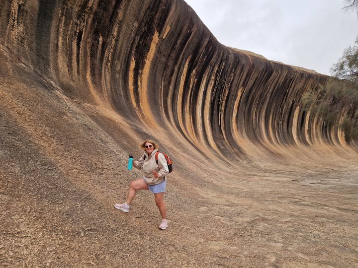Tourist posing in front of the iconic striped rock formation of Wave Rock.